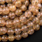 May include: A strand of golden rutilated quartz beads. The beads are round and translucent with gold inclusions. The beads are arranged in a pile, showing the variation in the size and shape of the beads.
