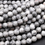 May include: A close-up of a pile of round, gray and white, marbled, gemstone beads. The beads are smooth and have a natural, organic look.