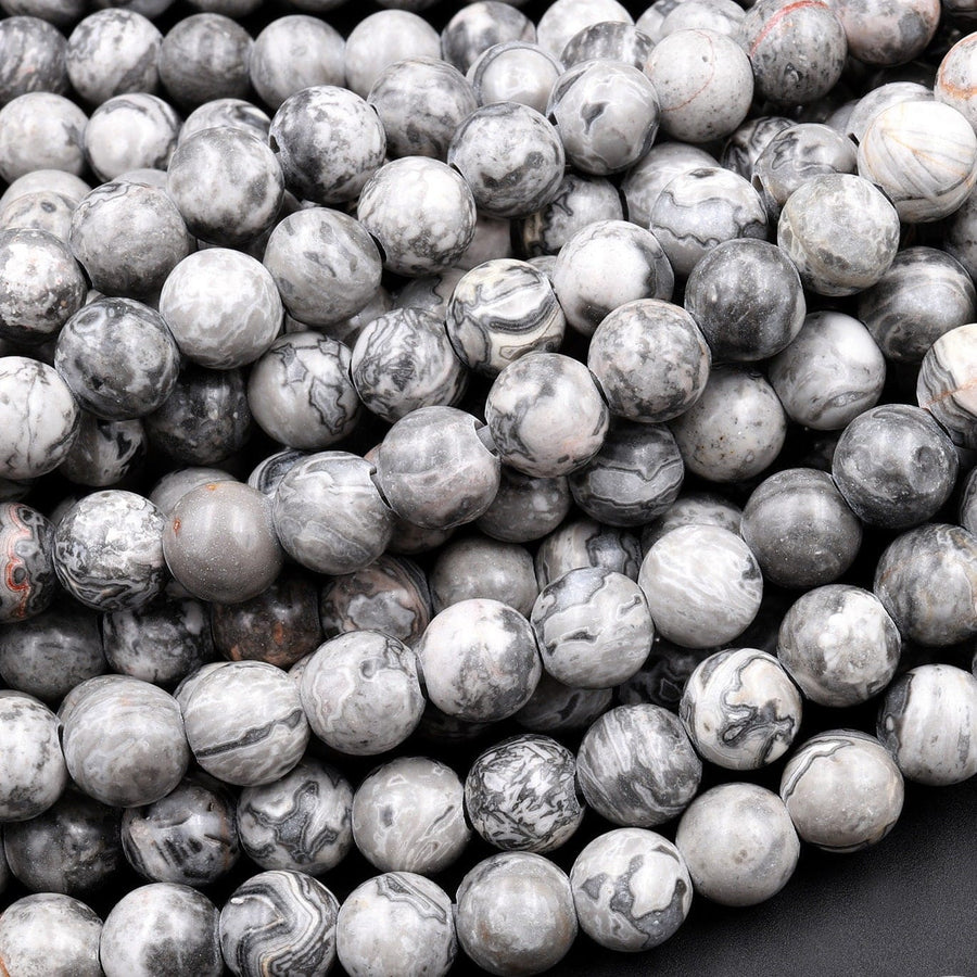 May include: A close-up of a pile of round, gray and white, marbled, gemstone beads. The beads are smooth and have a natural, organic look.