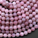 May include: A close-up image of a strand of pink gemstone beads. The beads are round and smooth, with a light pink color. The beads are arranged in a random pattern, and some of the beads have a slight shimmer to them.