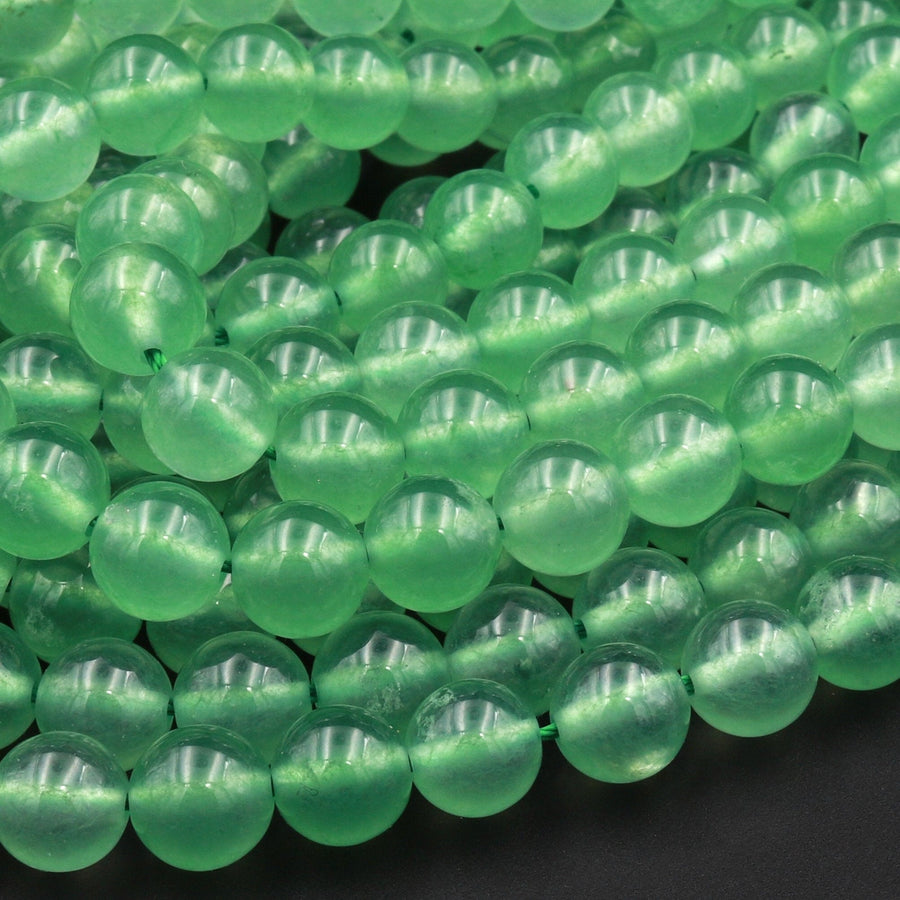 May include: A strand of smooth, round, green jade beads. The beads are translucent and have a slight shimmer. The beads are arranged in a loose pile, showing the individual beads.