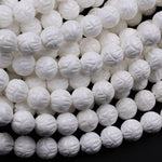 May include: A close-up image of a strand of white carved beads. The beads are round and have a floral design carved into them. The beads are arranged in a pile, showing the intricate detail of the carving.