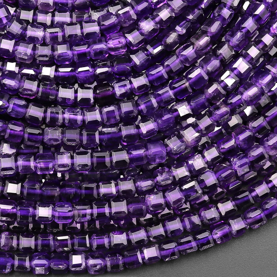 May include: A close-up image of a strand of purple amethyst gemstone beads. The beads are square shaped and have a faceted finish. The beads are arranged in a row, with the edges of the beads overlapping slightly. The beads are a deep purple color, with some lighter purple and white inclusions visible.