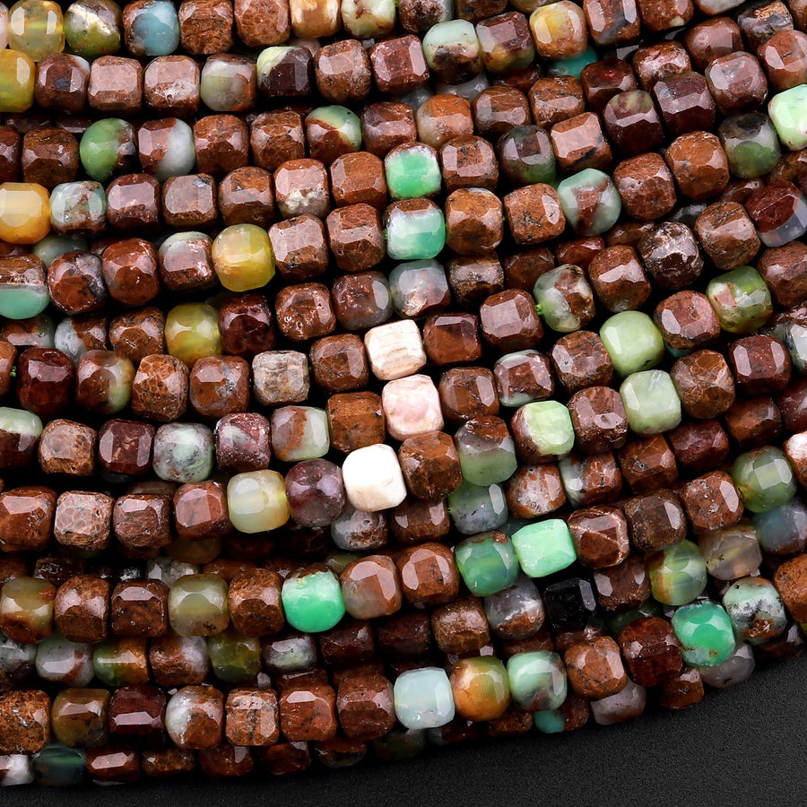 May include: Close-up of a strand of brown, green, and white gemstone beads. The beads are square-shaped and have a rough, textured surface. The beads are arranged in a random pattern, creating a visually appealing and unique look.