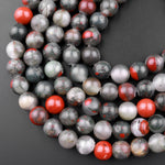 May include: A strand of round, gray and red gemstone beads. The beads are translucent and have a speckled pattern. The beads are arranged in a circular pattern, with the red beads interspersed throughout the gray beads.