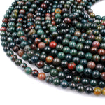 May include: A strand of green, red, and brown round gemstone beads. The beads are smooth and polished. The beads are arranged in a circular pattern.