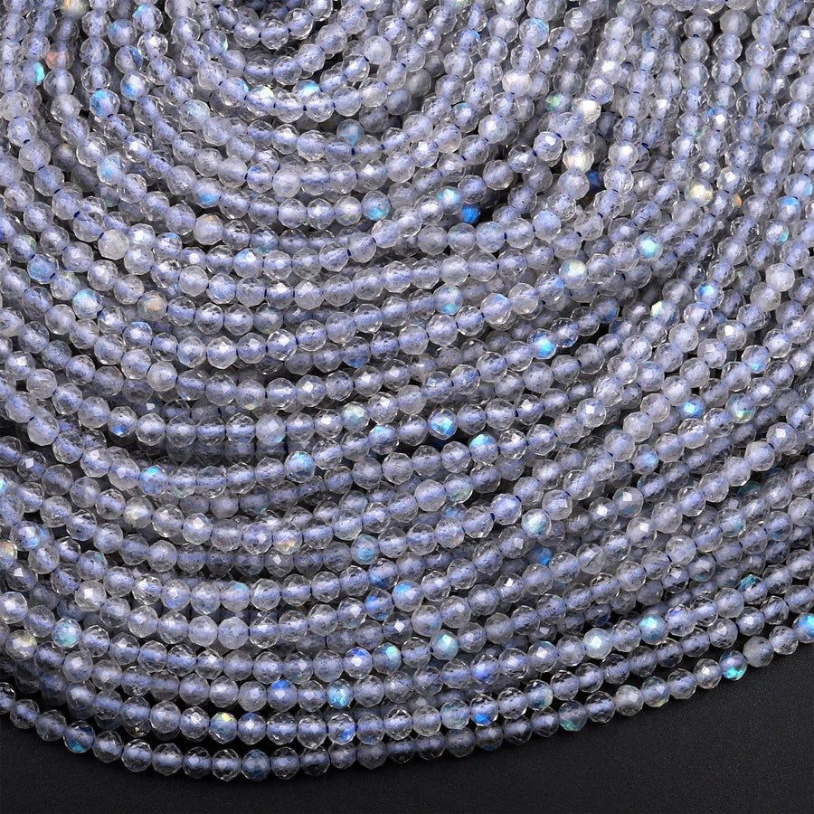 May include: A close-up image of a strand of light blue faceted gemstone beads. The beads are small and round, with a smooth, polished surface. The beads are arranged in a tight, overlapping pattern, creating a textured and iridescent effect.