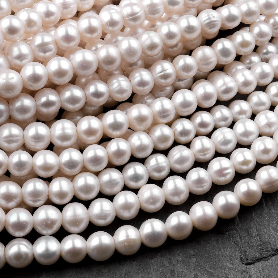 May include: A strand of white pearl beads. The pearls are round and smooth, and they are arranged in a close-up view. The pearls are all the same size and shape, and they are strung together on a thin, white thread.
