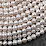 May include: A close-up of a strand of white pearl beads. The pearls are smooth and round, and they are arranged in a random pattern. The pearls are all the same size and shape, and they are all a creamy white color.