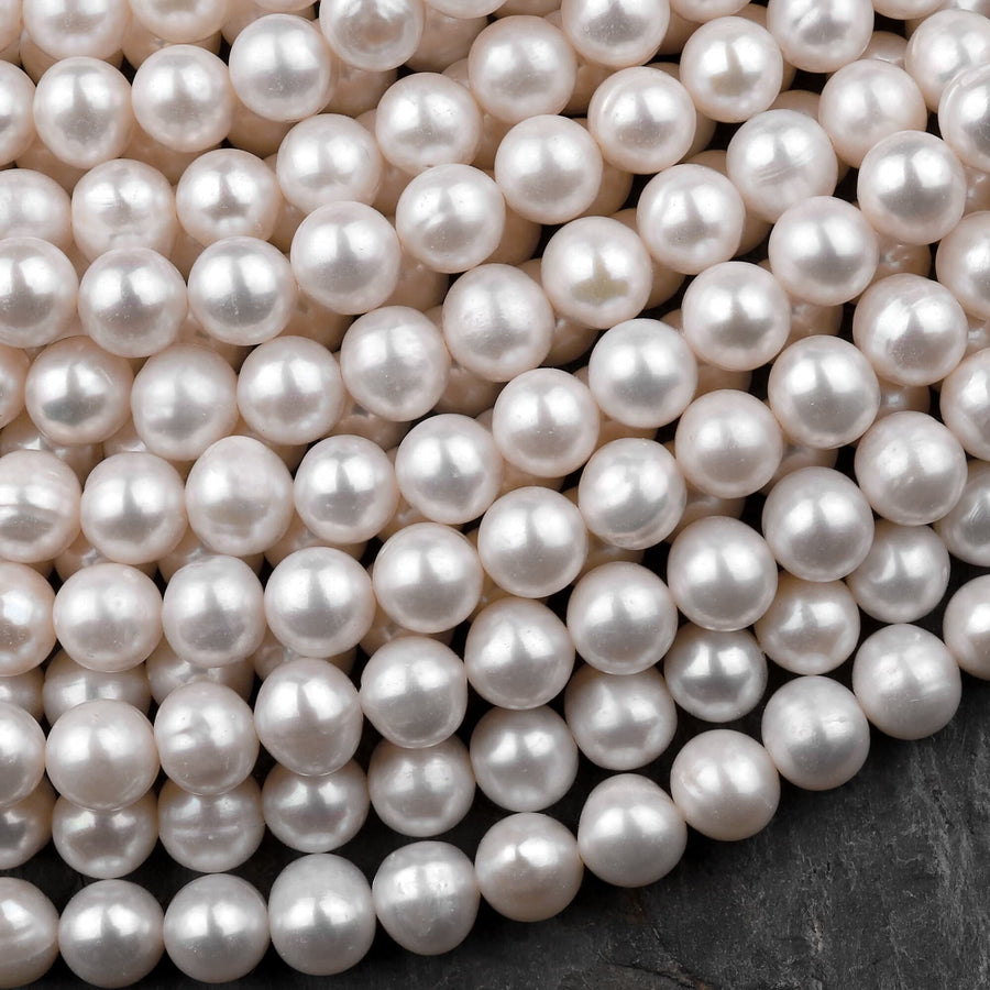 May include: A close-up of a strand of white pearl beads. The pearls are smooth and round, and they are arranged in a random pattern. The pearls are all the same size and shape, and they are all a creamy white color.