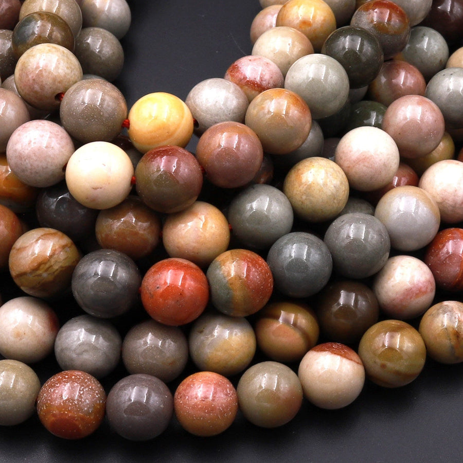 May include: A close-up of a pile of round, smooth, multicolored gemstone beads. The beads are various shades of brown, gray, white, red, and yellow. The beads are polished and have a natural, organic look.