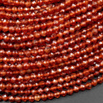 May include: A strand of faceted garnet beads. The beads are a deep reddish-orange color and have a glossy finish. The beads are arranged in a close-up view, showing the intricate facets of each bead.