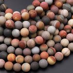 May include: A close-up image of a strand of round, multi-colored gemstone beads. The beads are a mix of brown, gray, white, and red with various patterns and textures. The beads are arranged in a pile, showing the different colors and patterns.