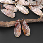 May include: Two teardrop shaped agate pendants with brown string attached. The agate is a mix of white, brown, red, and orange colors with a swirling pattern.