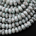 May include: A close-up of a pile of white and green speckled beads. The beads are round and have a smooth, polished surface. The beads are arranged in a random pattern and are illuminated by a bright light source. The beads are likely made of natural stone or glass.