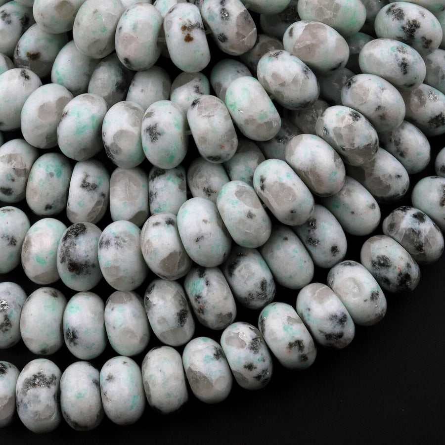 May include: A close-up of a pile of white and green speckled beads. The beads are round and have a smooth, polished surface. The beads are arranged in a random pattern and are illuminated by a bright light source. The beads are likely made of natural stone or glass.