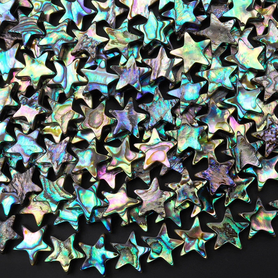 May include: A collection of iridescent star-shaped beads. The beads display a range of colors including teal, purple, and gold. Each bead has a five-point star shape with a glossy, reflective surface. The beads are scattered, creating a dense, textured pattern. These beads are suitable for jewelry making or craft projects.