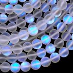 May include: A strand of iridescent white glass beads. The beads are round and have a frosted finish. The beads are arranged in a loose pile, with some of the beads overlapping each other. The beads are illuminated from the side, creating a soft, ethereal glow.