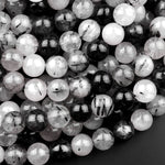 May include: A close-up of a pile of round black and white beads. The beads are made of clear quartz with black inclusions. The beads are smooth and shiny.