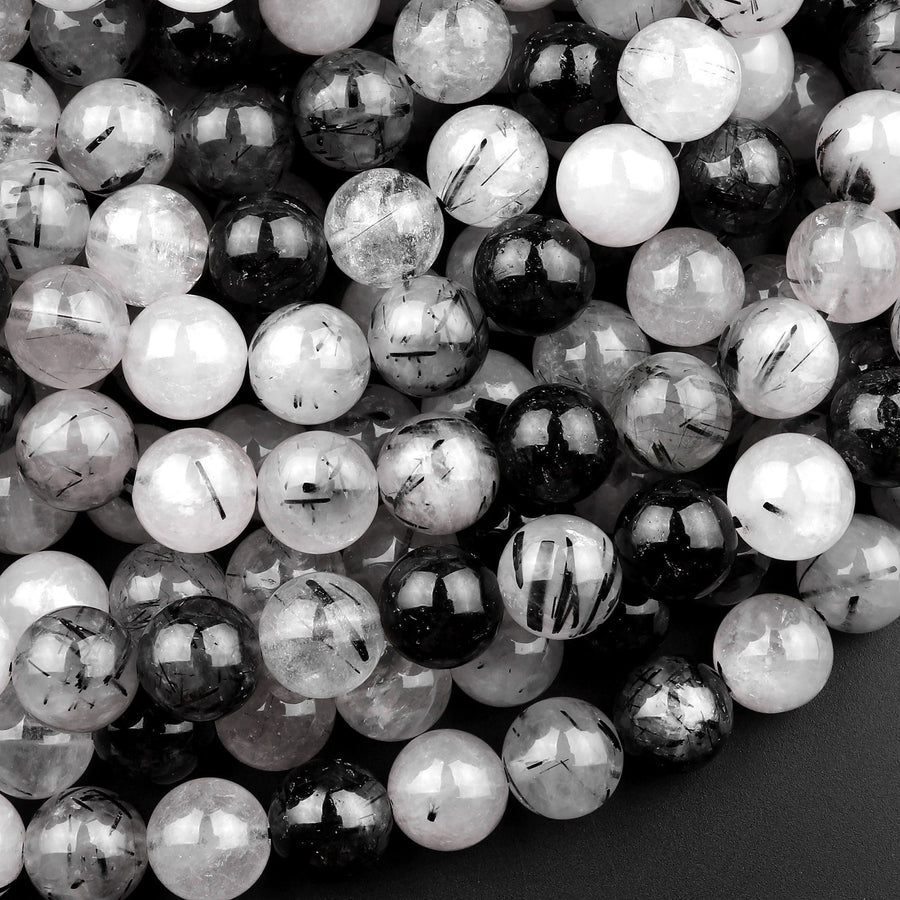 May include: A close-up of a pile of round black and white beads. The beads are made of clear quartz with black inclusions. The beads are smooth and shiny.