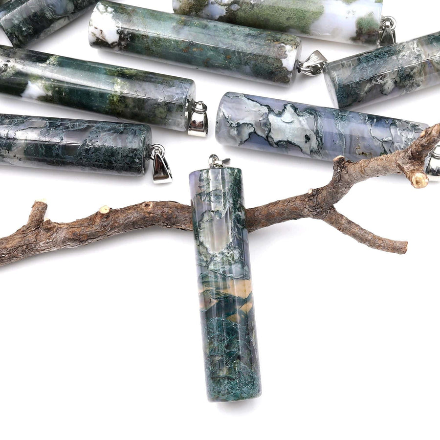 May include: A collection of green, gray, and white agate stone pendants with silver jump rings. The pendants are cylindrical in shape and have a variety of patterns and textures. The pendants are displayed on a branch against a white background.