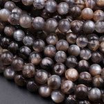 May include: A close-up image of a pile of round, black and silver sunstone beads. The beads are smooth and shiny, with a subtle shimmer. The beads are arranged in a random pattern, with some overlapping.