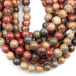 May include: A close-up of a strand of round, multi-colored gemstone beads. The beads are a mix of red, brown, green, and cream colors. The beads are smooth and polished, and they have a natural, organic look.