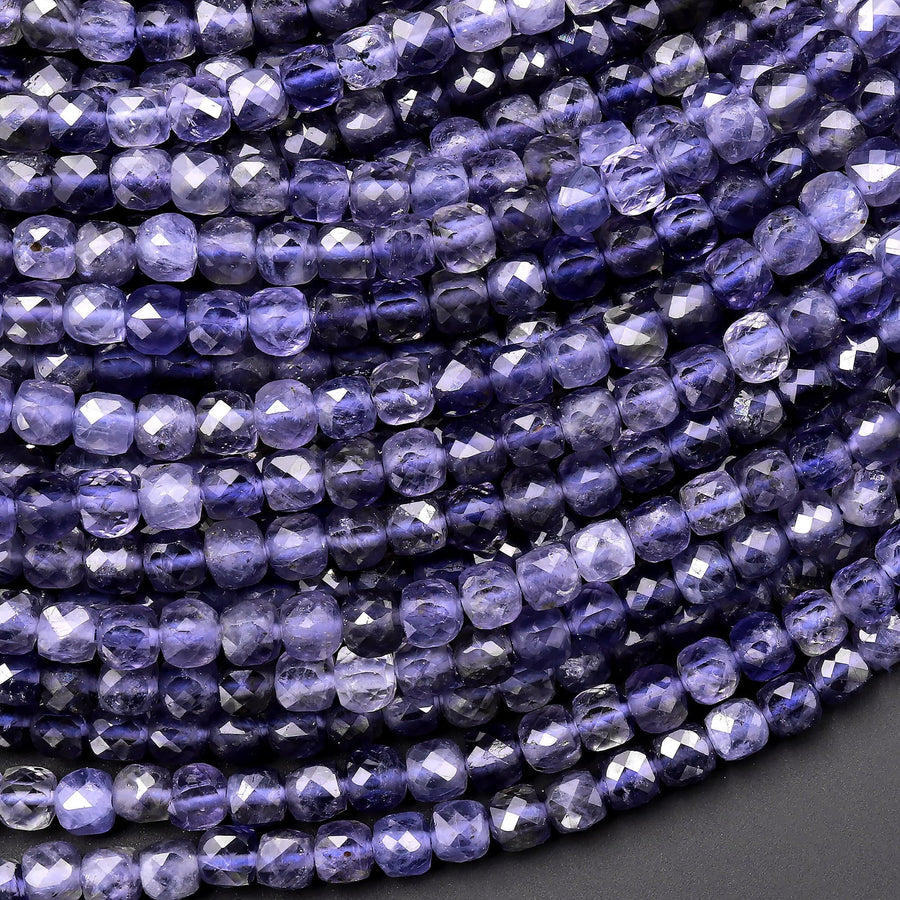 May include: Close-up of a collection of faceted, square-shaped beads in shades of deep purple and lavender. The beads are strung together, creating a textured surface. The beads are likely used for jewelry making.