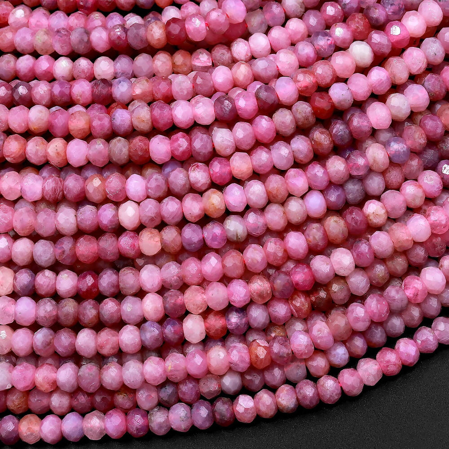 May include: A strand of pink ruby gemstone beads. The beads are faceted and have a slightly irregular shape. They are strung on a clear thread.