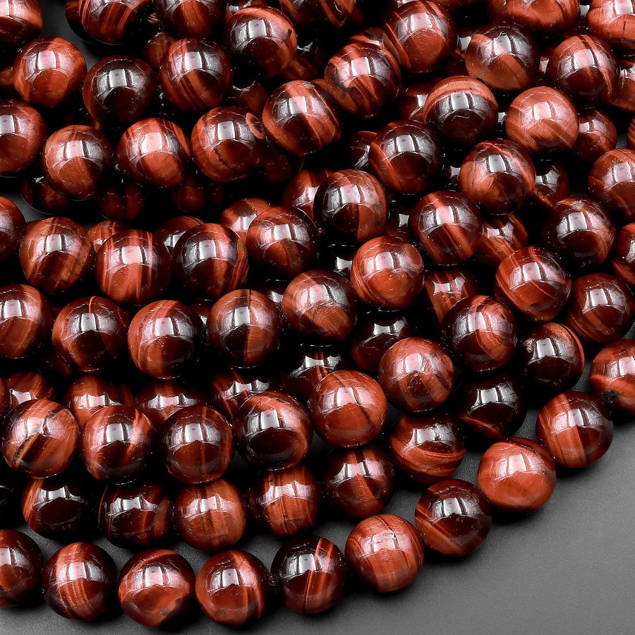 May include: A strand of red tiger's eye beads. The beads are round and have a smooth, polished finish. The red tiger's eye is a gemstone that is known for its unique chatoyancy, which is the shimmering effect that is visible when the stone is turned in the light.