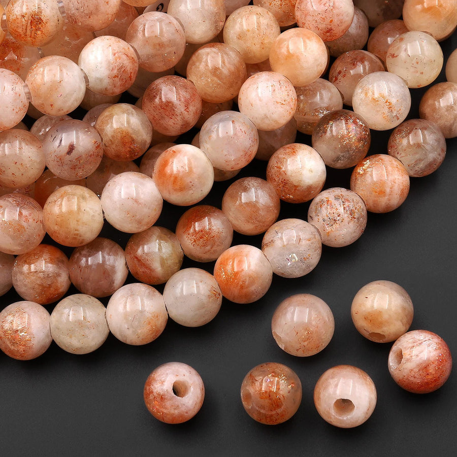 May include: A collection of round sunstone beads featuring a translucent, pale peach base color with internal shimmering copper-colored inclusions. Each bead has a smooth, polished surface and a central hole for stringing, displaying natural variations.