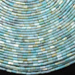 May include: Close-up of a collection of small, cylindrical beads in shades of blue, green, and white. The beads are arranged in curved rows, creating a textured, layered effect. The overall aesthetic is cool and calming.