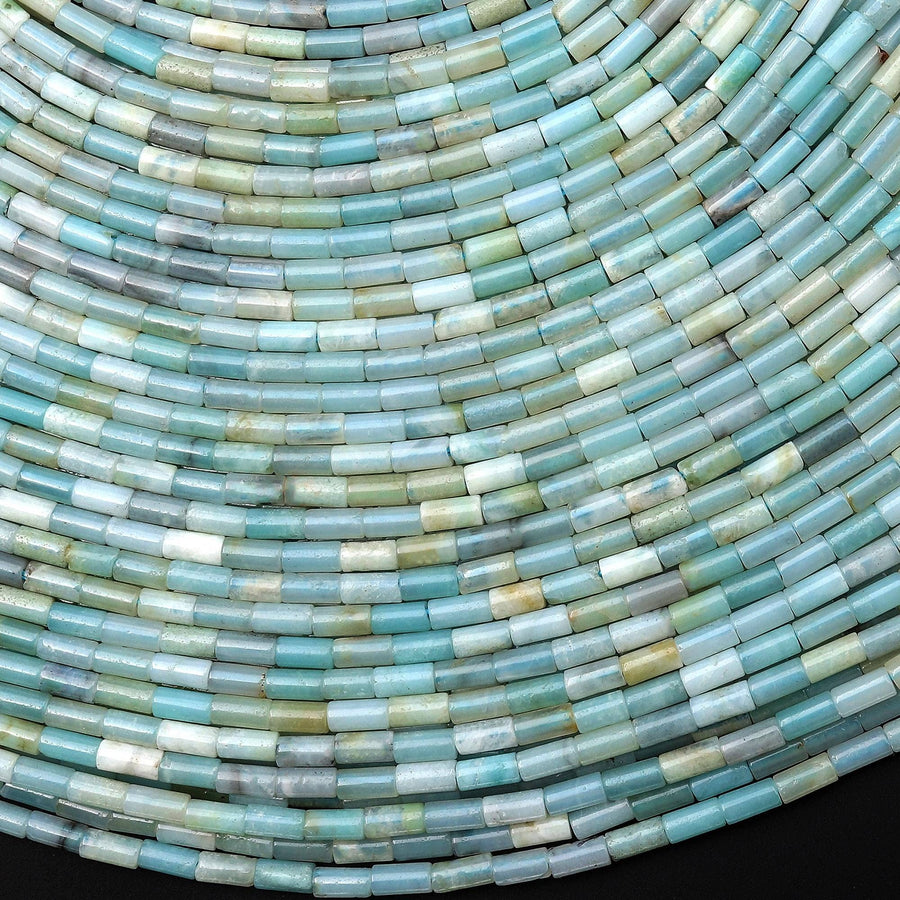 May include: Close-up of a collection of small, cylindrical beads in shades of blue, green, and white. The beads are arranged in curved rows, creating a textured, layered effect. The overall aesthetic is cool and calming.